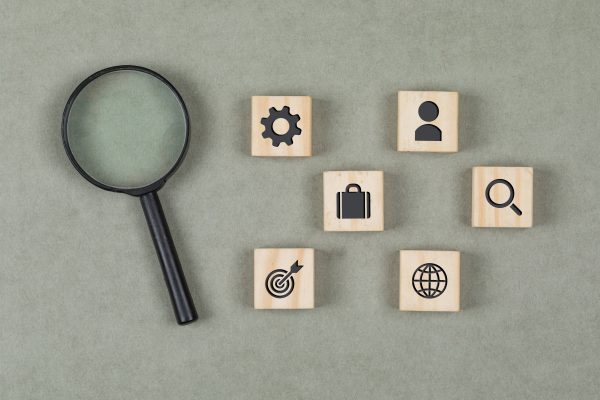 Financial Concept With Wooden Cubes, Magnifying Glass On Grey Background Flat Lay.
